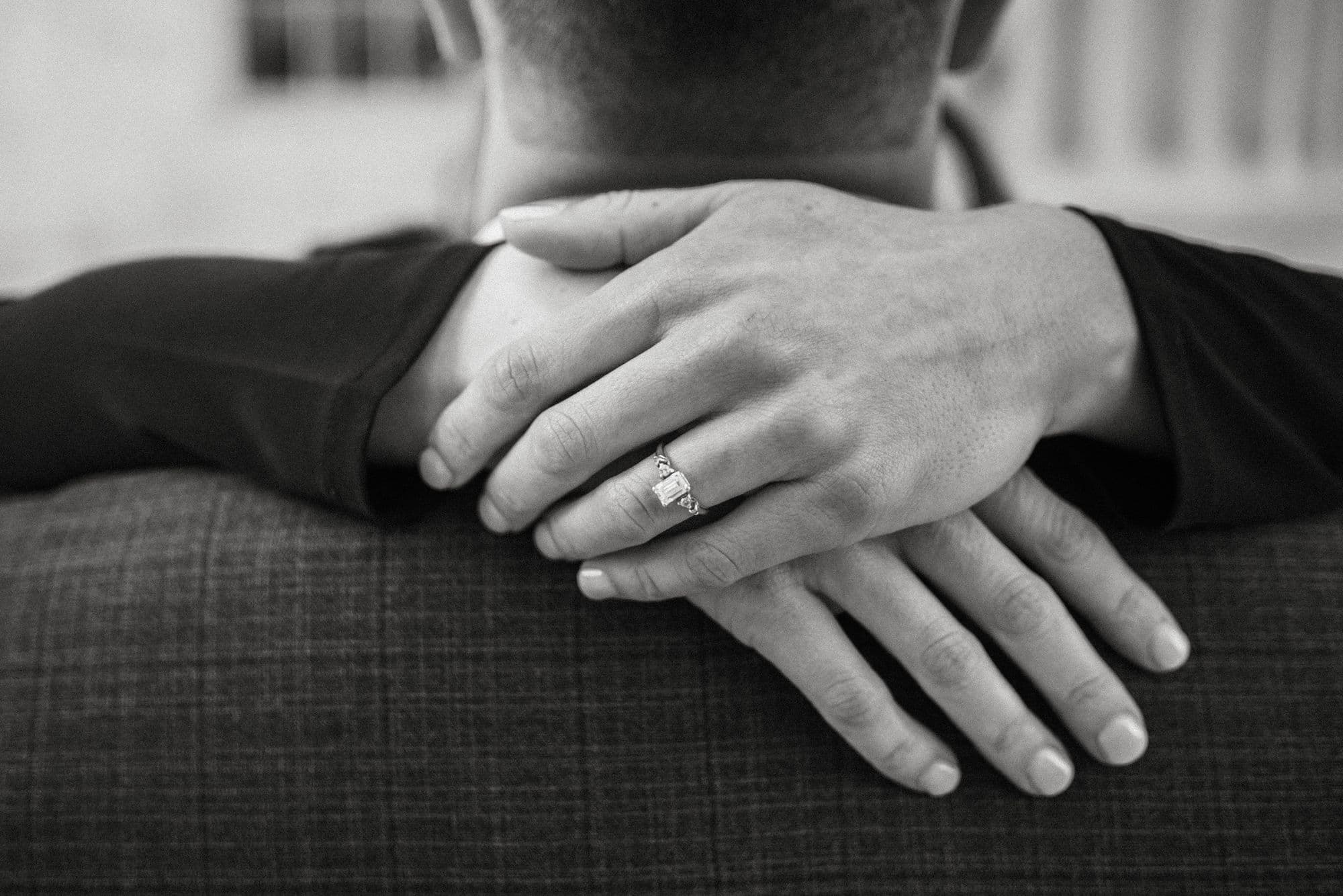 Two hands resting together, an engagement ring on one